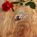 A sterling silver necklace with a single dark purple Edison floating pearl, displayed on a wooden surface next to a red rose.