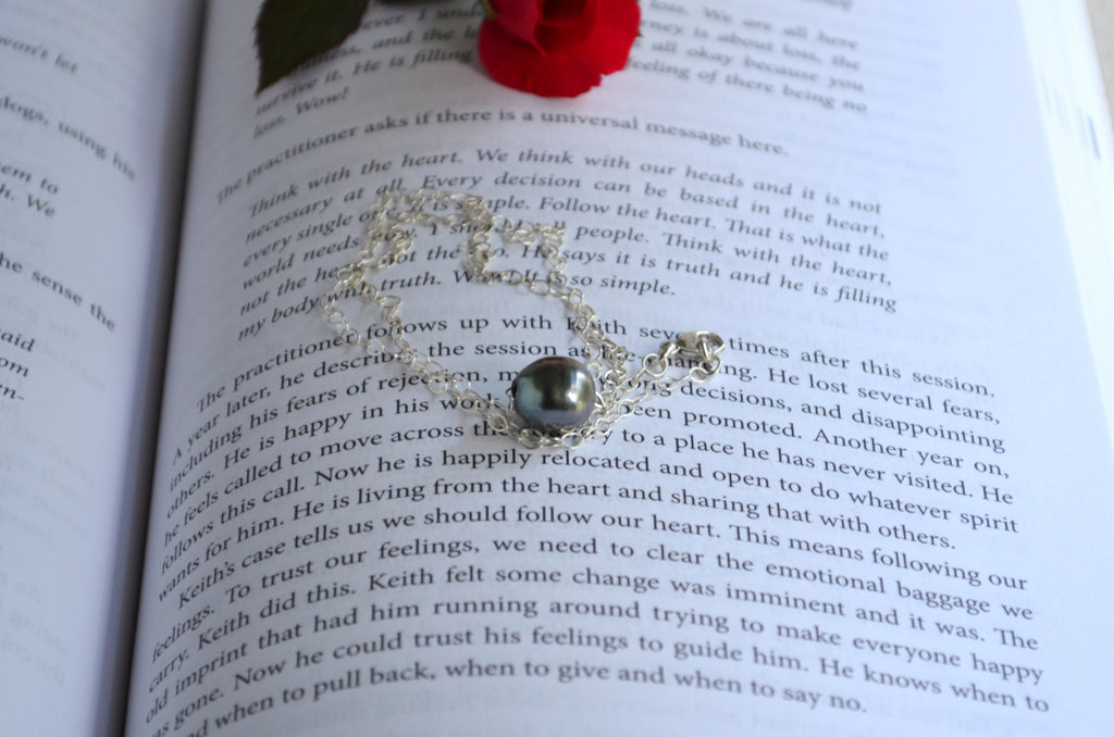 A silver-toned necklace with a round dark green stone is draped over an open book page with printed text.