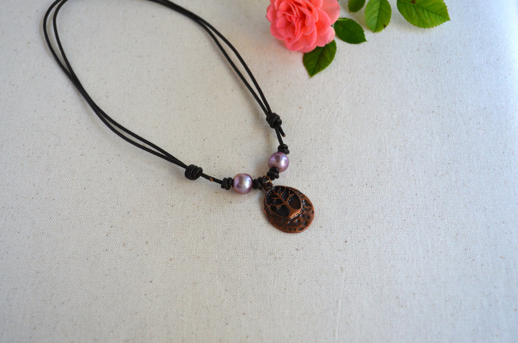 Necklace with two pink Edison pearls and Tree of life pendant on brown Greek leather cord on the light fabric background with pink rose on the back