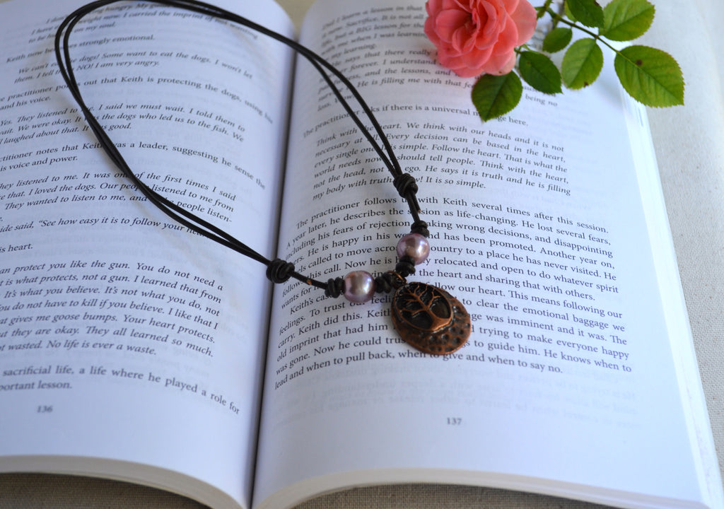 Necklace with two pink Edison pearls and Tree of life pendant on brown Greek leather cord on the book background with pink rose on the back