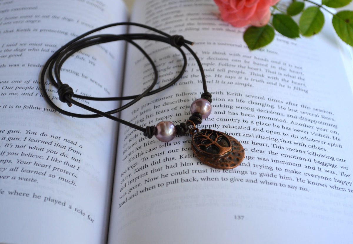 Necklace with two pink Edison pearls and Tree of life pendant on brown Greek leather cord on the book background with pink rose on the back