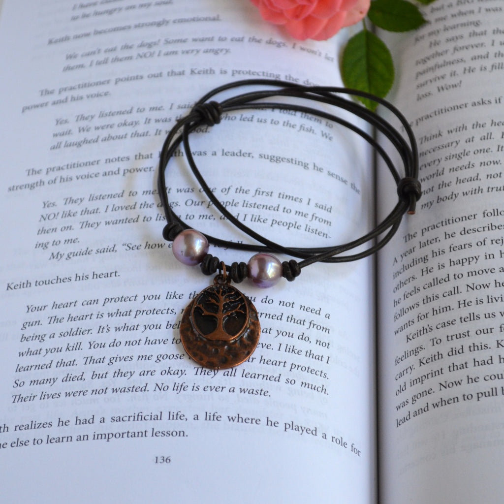 Necklace with two pink Edison pearls and Tree of life pendant on brown Greek leather cord on the book background with pink rose on the back
