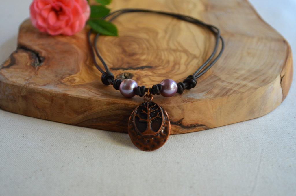 Necklace with two pink Edison pearls and Tree of life pendant on brown Greek leather cord on the wooden surface with pink rose on the back