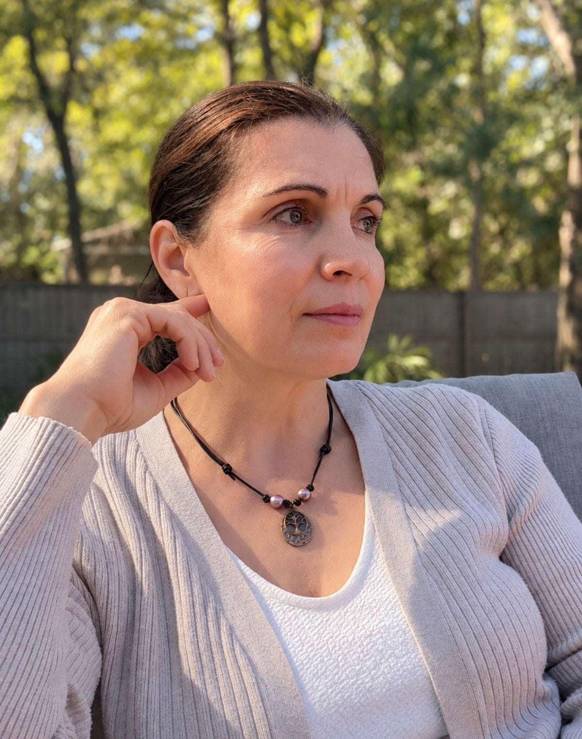 A person outdoors wearing leather necklace with two pink pearls and tree of life pendant