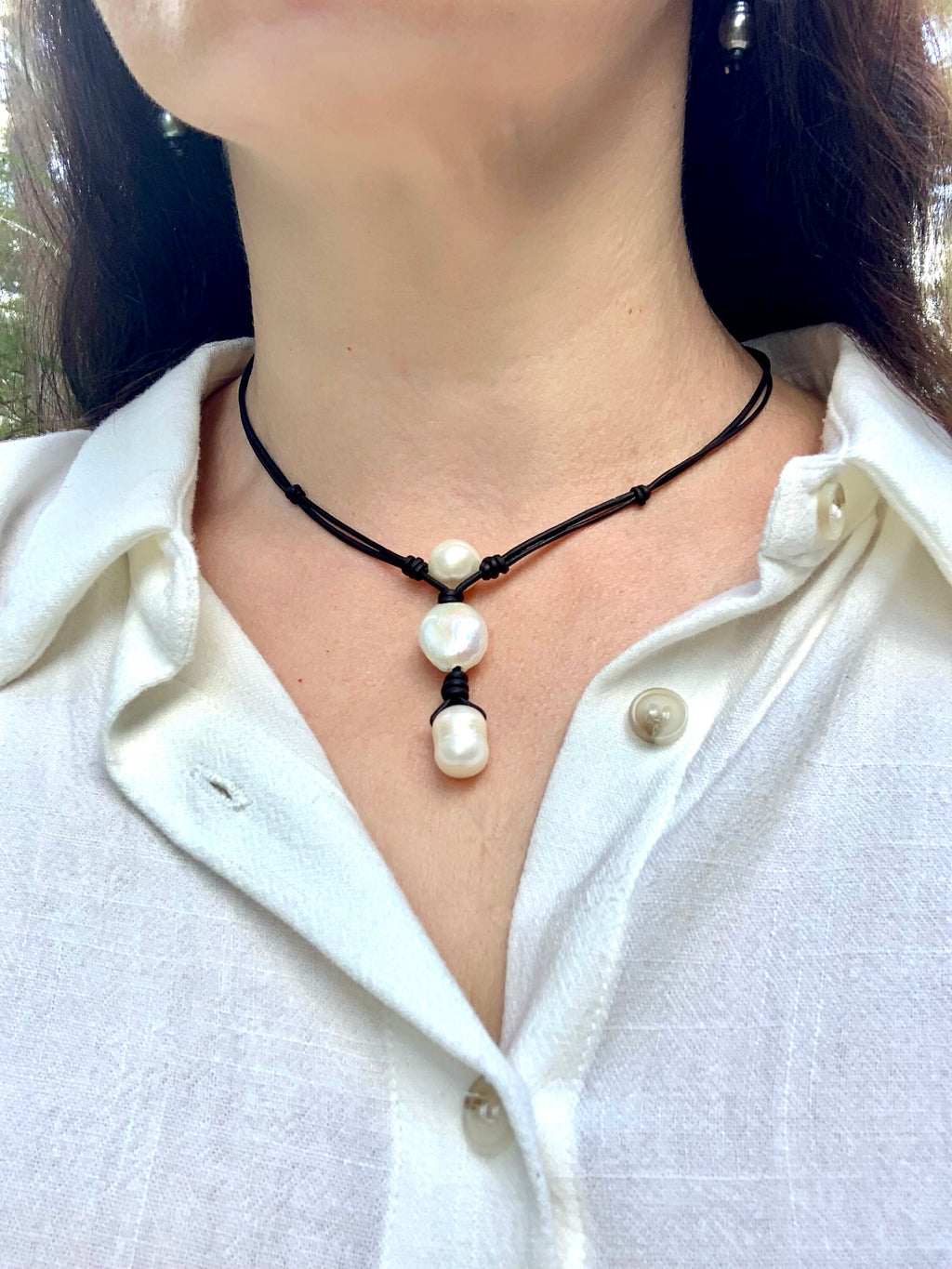 Person wearing a necklace with pearl pendants on a white shirt.