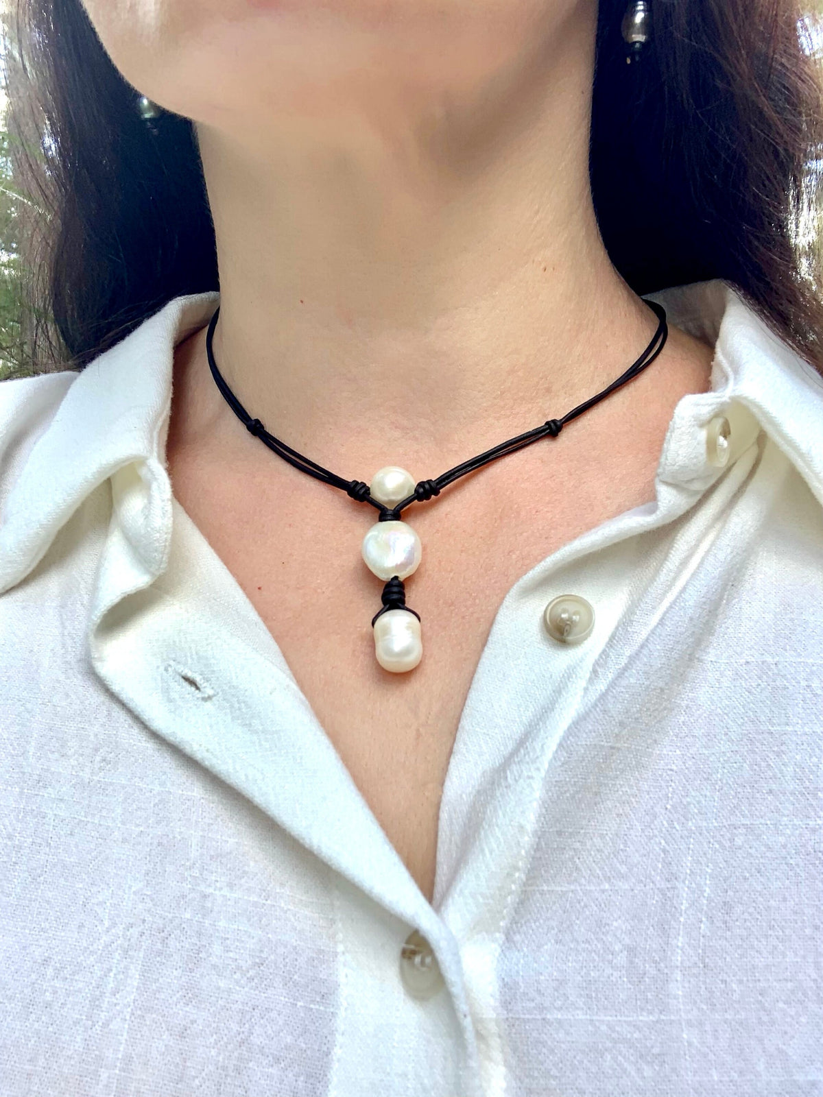Person wearing a necklace with pearl pendants on a white shirt.