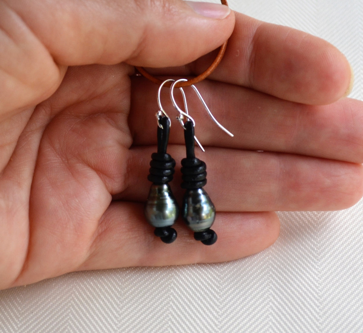 Hand holding a pair of black Tahitian pearls beaded earrings on a white background