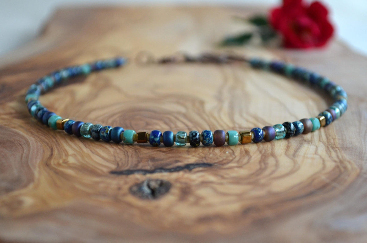 Beaded necklace on a wooden surface with a red flower in the background