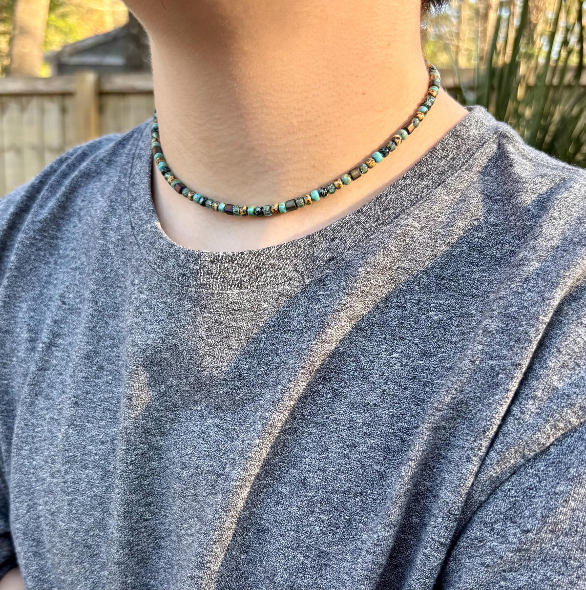 Person wearing a beaded necklace with a blurred outdoor background