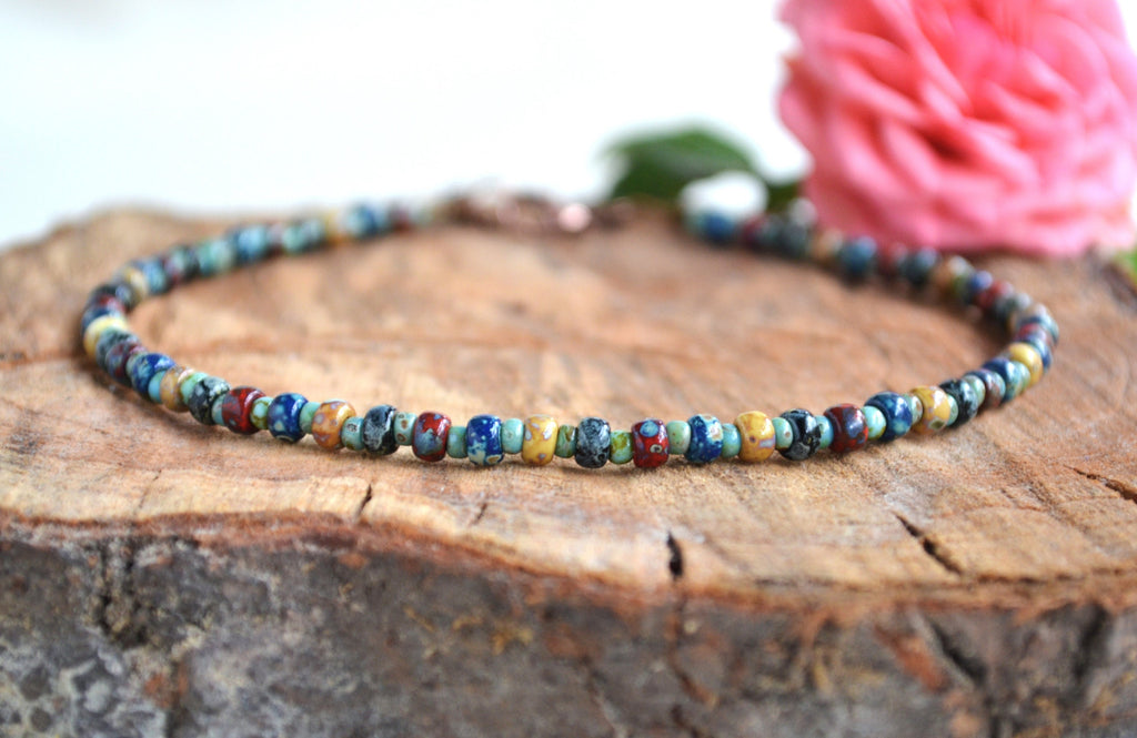 Multicolored beaded anklet on a wooden surface with a pink flower in the background
