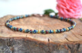 Multicolored beaded anklet on a wooden surface with a pink flower in the background