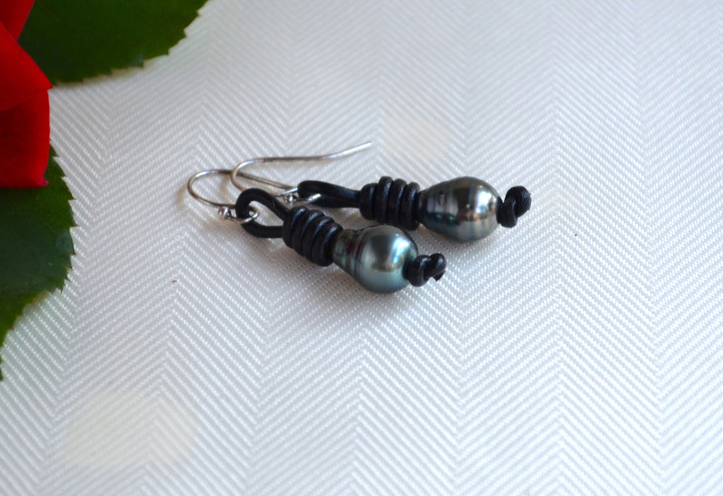 Pair of black Tahitian pearls beaded earrings on a textured white surface with a red flower in the corner.