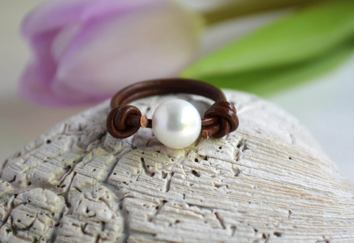 Pearl on leather ring on a textured surface with a blurred floral background