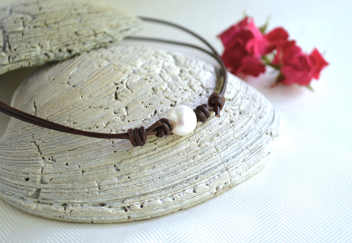Necklace with a pearl pendant on a textured surface with pink flowers in the background