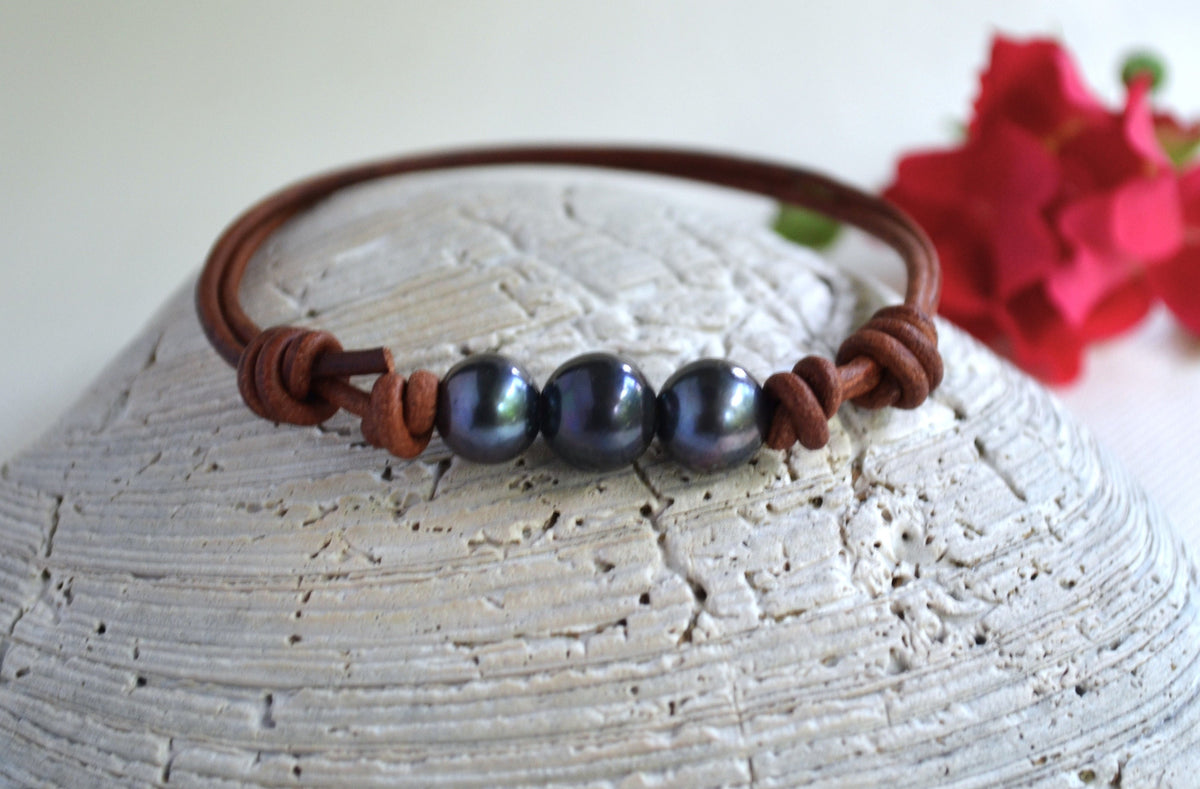 Bracelet with dark pearls on brown leather strap on a textured surface with a red flower in the background