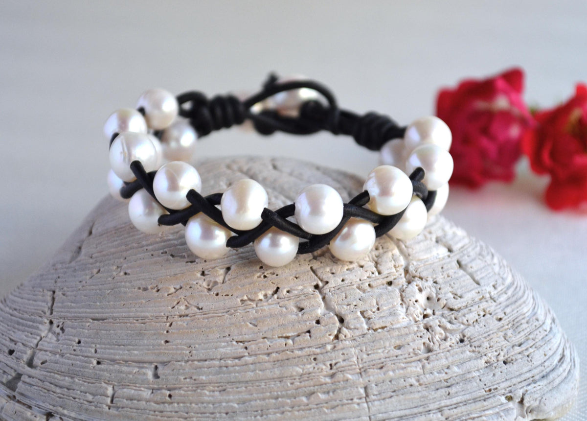 Pearl bracelet with black cord on a textured surface with red flowers in the background
