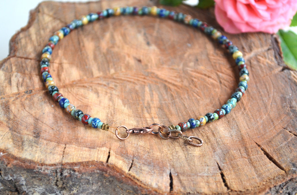 Multicolored beaded anklet on a wooden surface with a pink flower in the background