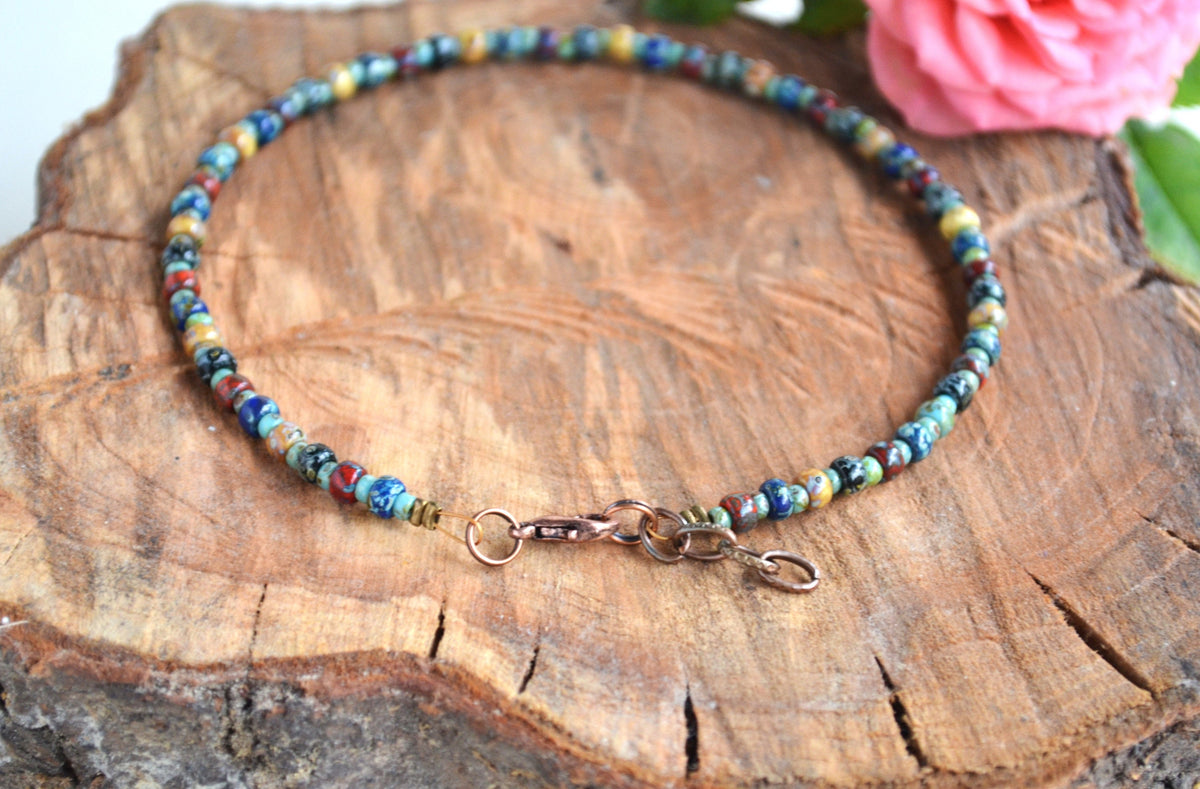 Multicolored beaded anklet on a wooden surface with a pink flower in the background