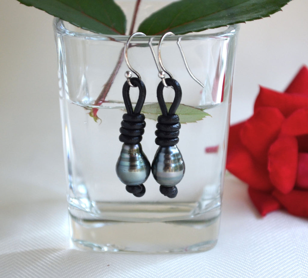 Black Tahitian pearls and sterling silver beaded earrings in a clear glass with a red flower and green leaves in the background.