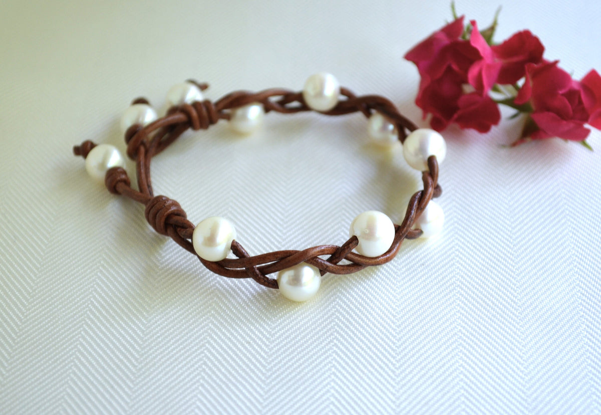 Bracelet with brown cord and white pearls on a white background with red flowers.