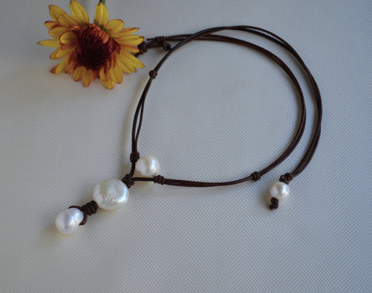 Necklace with pearls on a brown cord next to a yellow flower on a light gray background