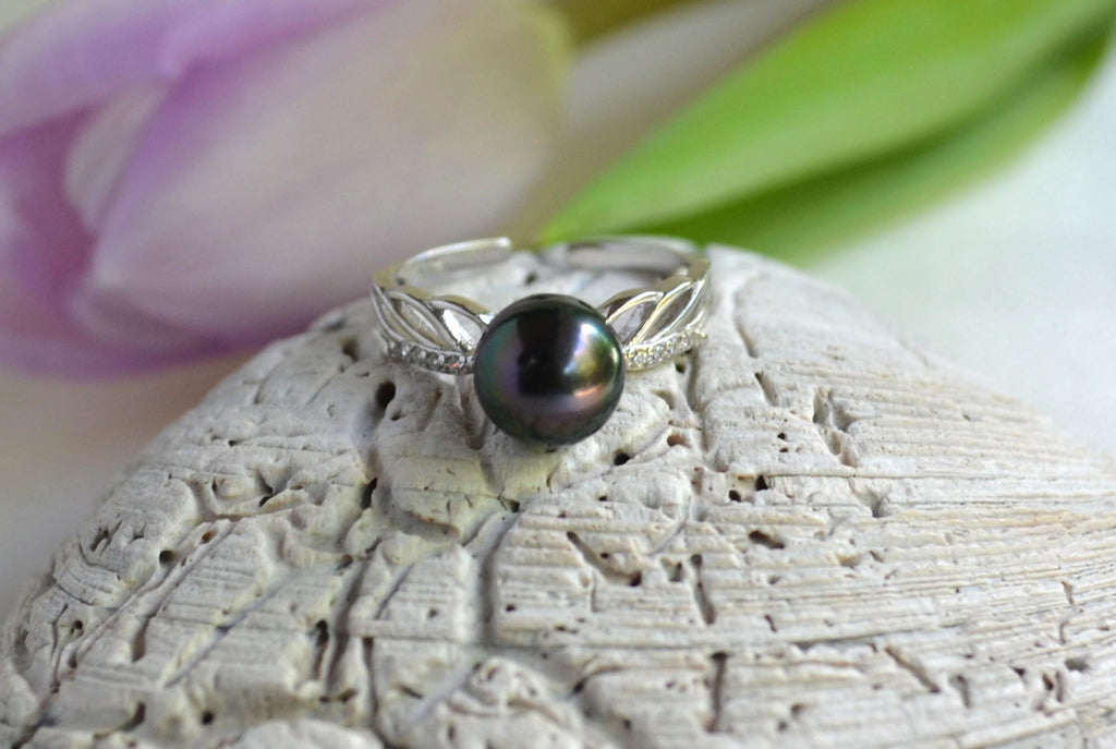 Silver ring with a black pearl on a textured stone surface with blurred flowers in the background