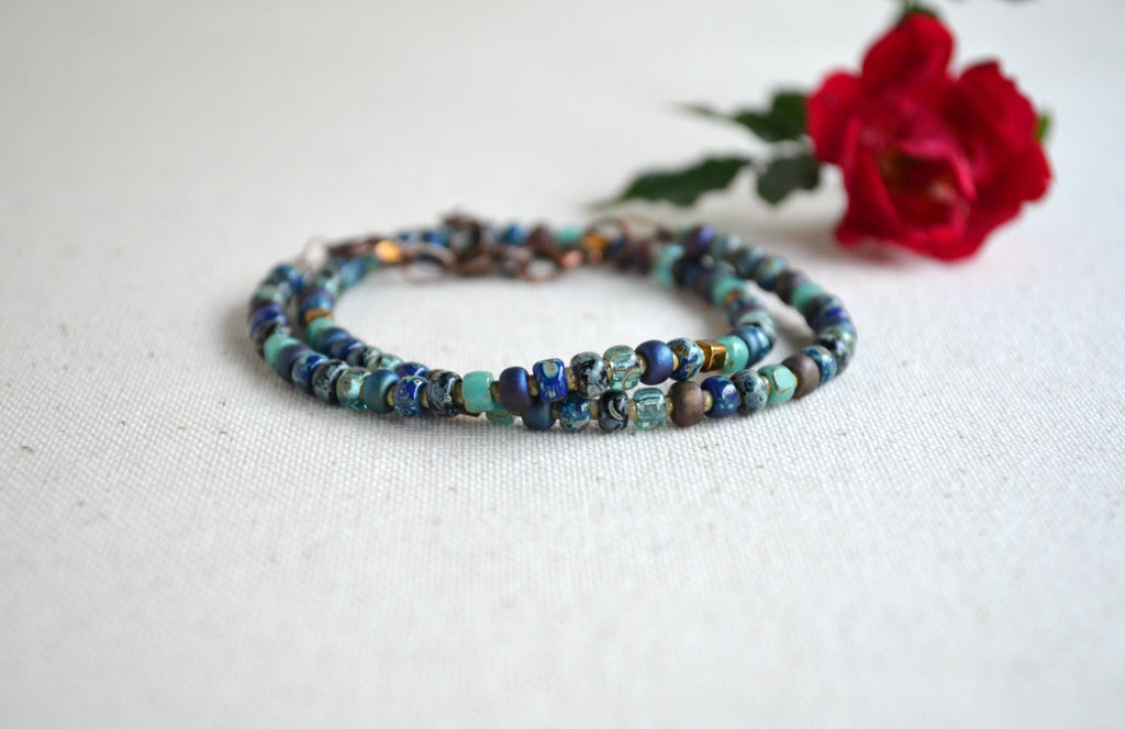 Multicolored beaded necklace on a white surface with a red rose.