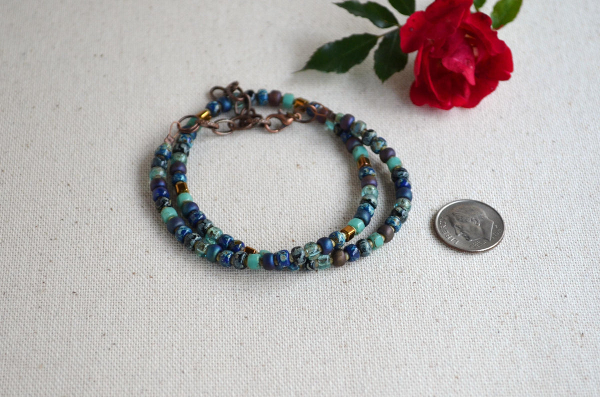 Multicolored beaded necklace on a light fabric background with a red rose.