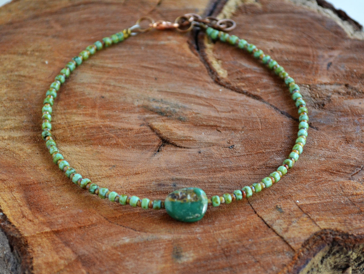 Green beaded ankle bracelet with a large Turquoise stone on a wooden surface