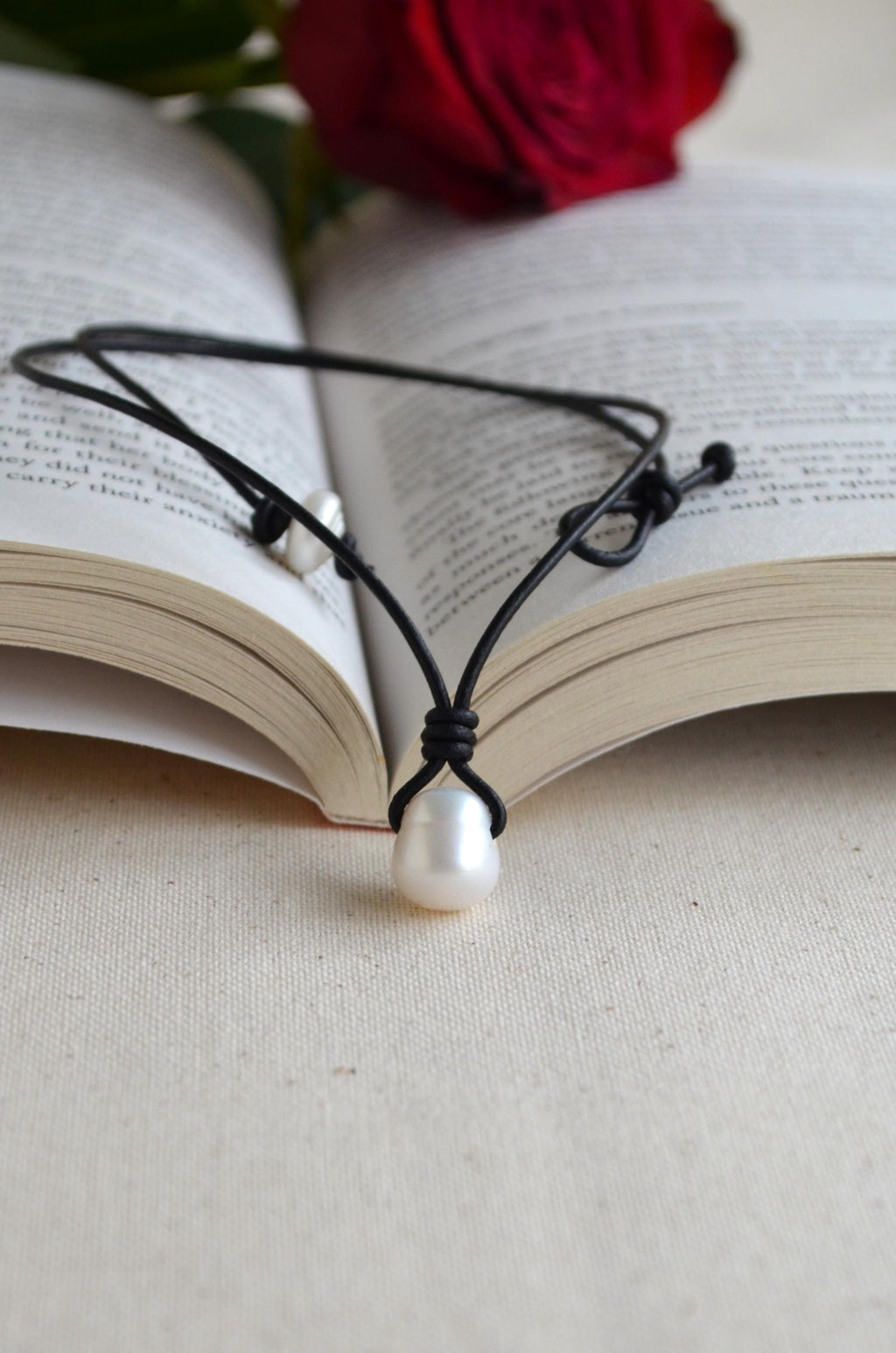 Pearl necklace on an open book with a red rose in the background
