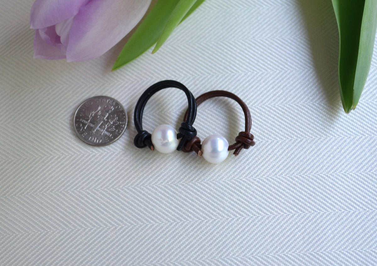 Two pearl leather rings on a textured surface with a coin for scale, next to a purple tulip.