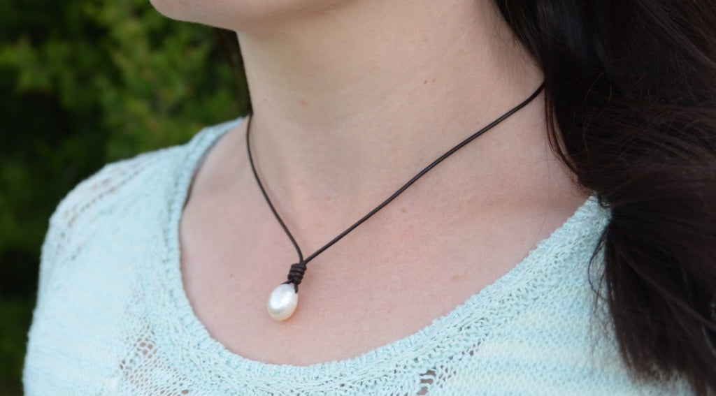 Person wearing a necklace with a pearl pendant outdoors