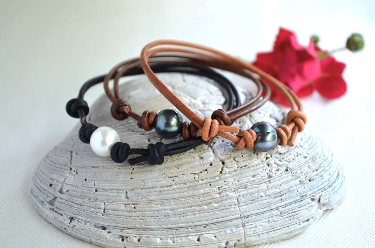 Three leather bracelets with beads on a textured stone surface with a pink flower in the background.