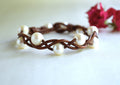 Bracelet with white pearls and brown braided band on a white background with red flowers.