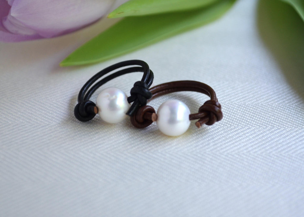 Two pearl leather rings on a textured surface with a blurred floral background
