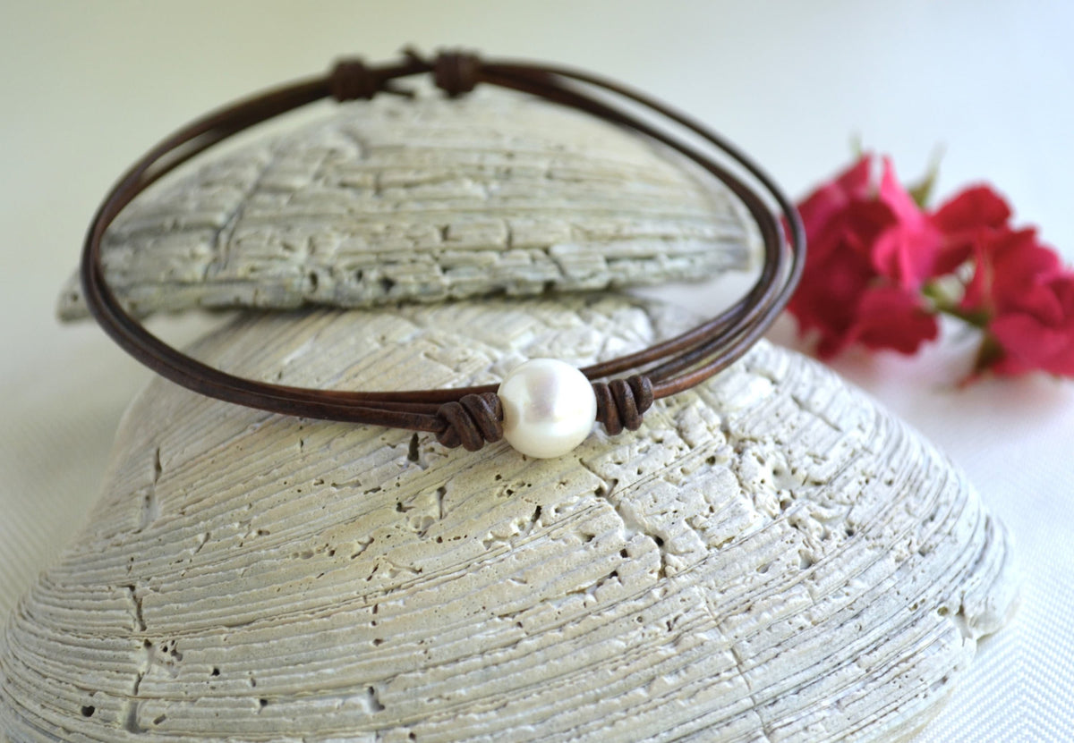Brown leather choker with a pearl on a textured surface with flowers in the background