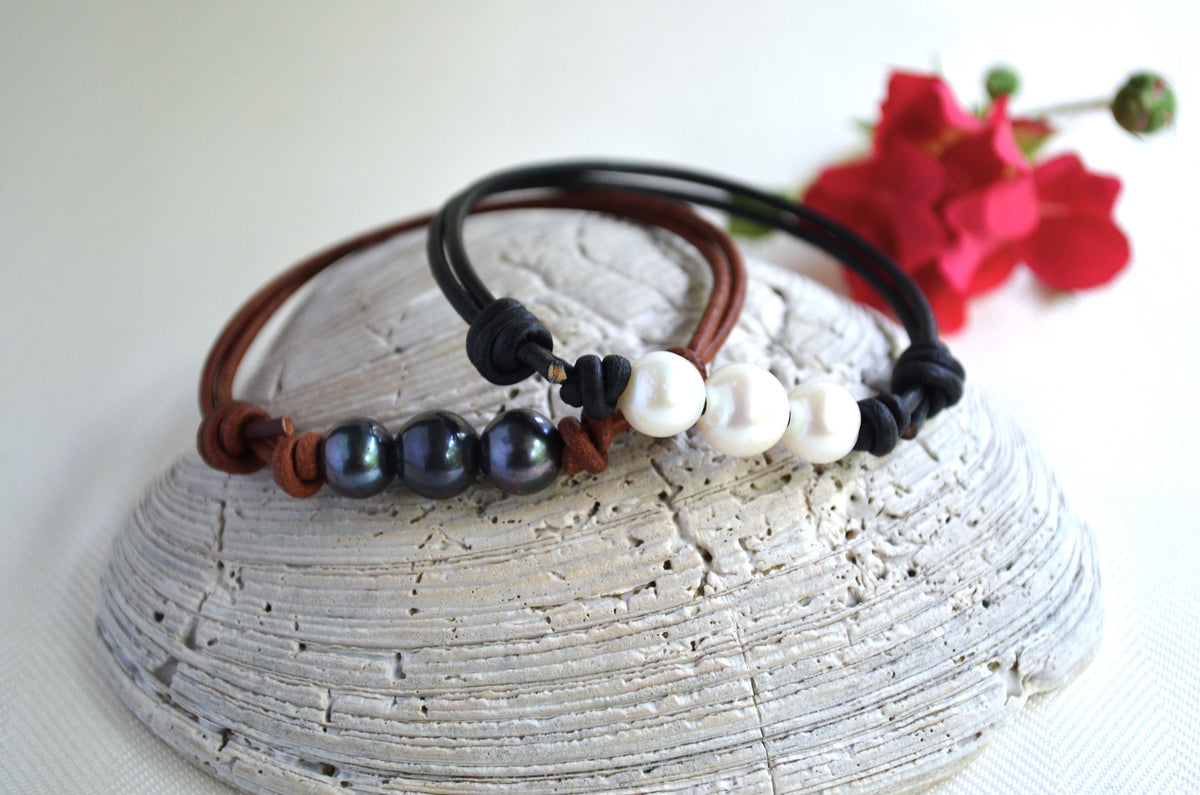 Two bracelets with freshwater pearls on a textured white surface with a red flower in the background