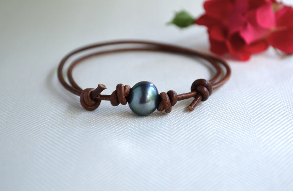 Bracelet with a dark pearl bead on a white background with a red flower.