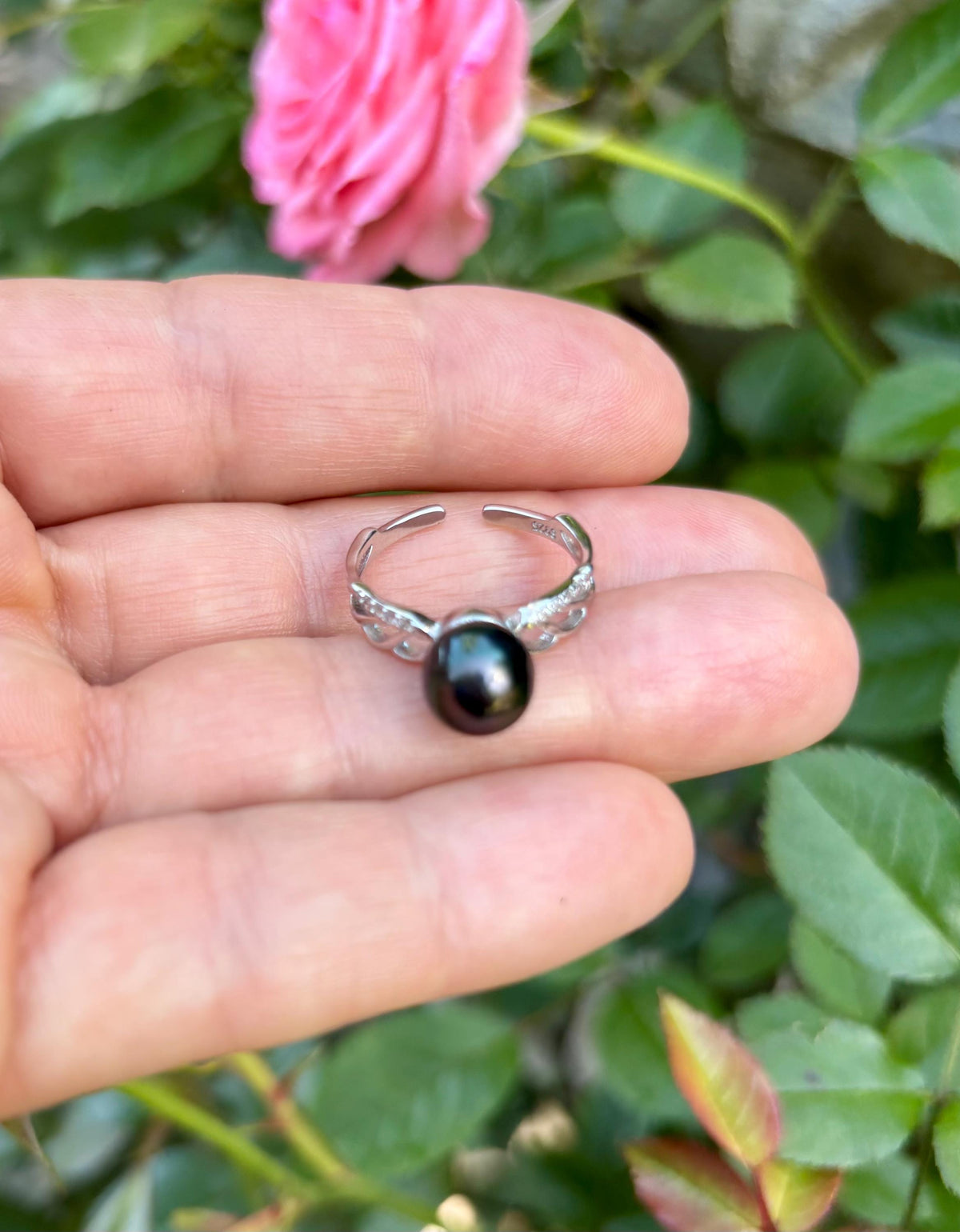 Sterling silver ring with Tahitian Pearl held in a hand against a blurred floral background