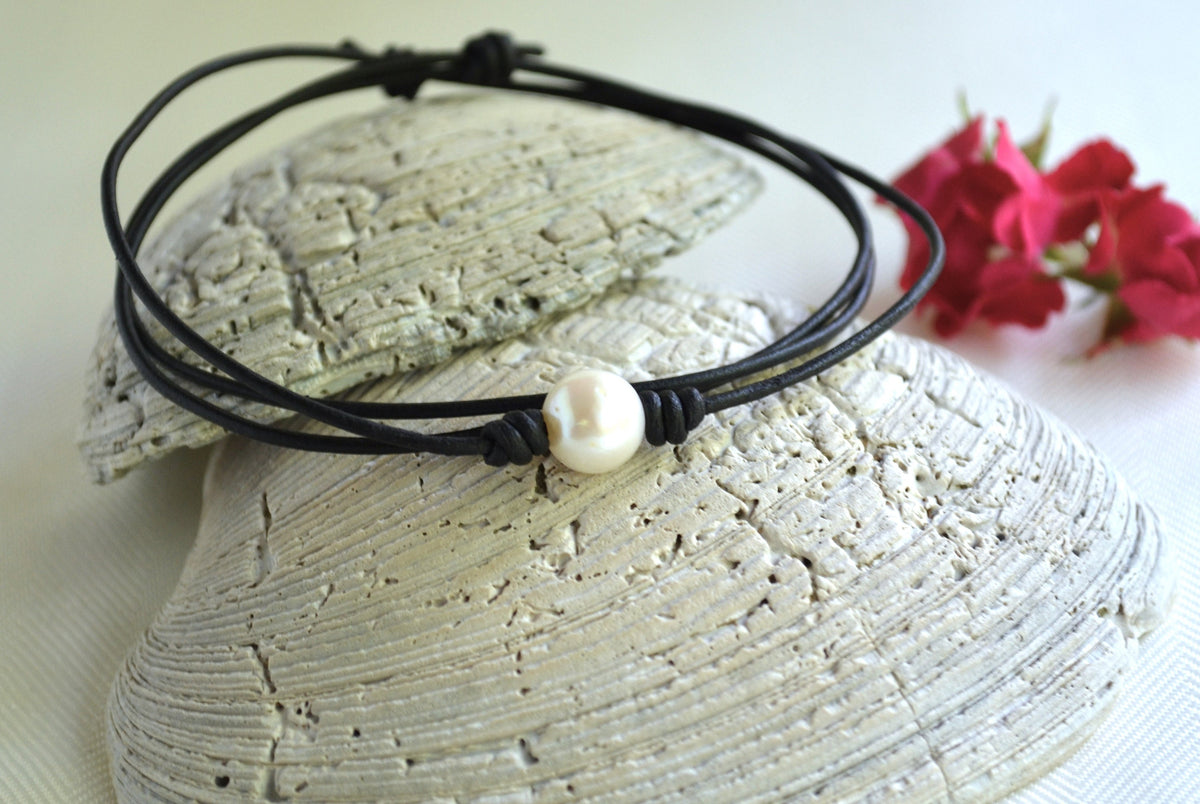 Black leather choker with a pearl bead on a stone surface with pink flowers in the background