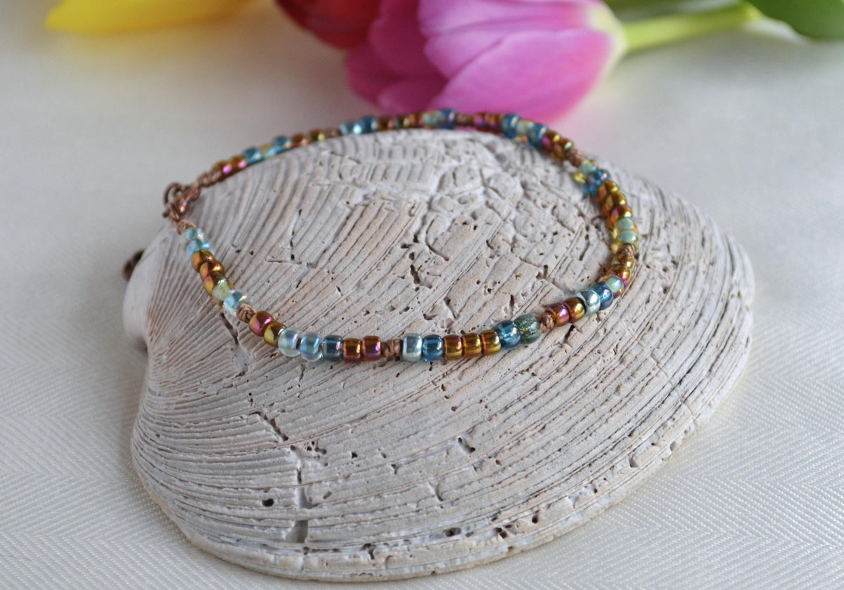 Multicolored beaded ankle bracelet on a shell with flowers in the background