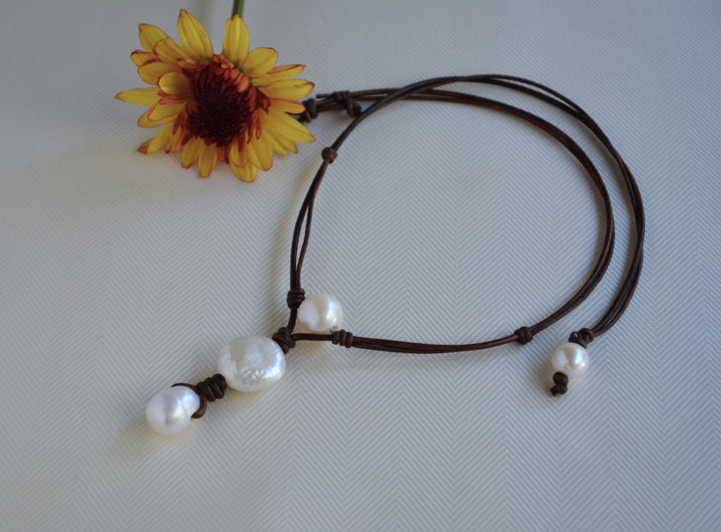 Necklace with pearls on a brown cord next to a yellow flower on a light gray background
