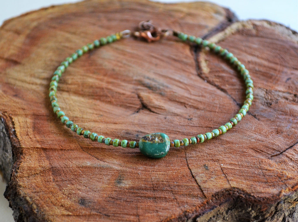 Green beaded ankle bracelet with a large turquoise stone on a wooden surface