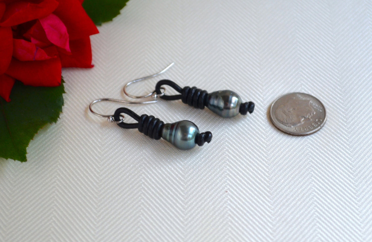 Pair of black Tahitian pearls earrings with on a white surface next to a red flower and coin for scale.