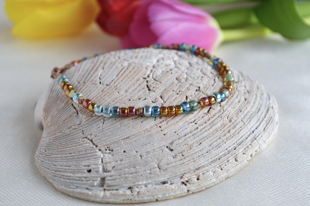 Multicolored beaded ankle bracelet on a shell with flowers in the background