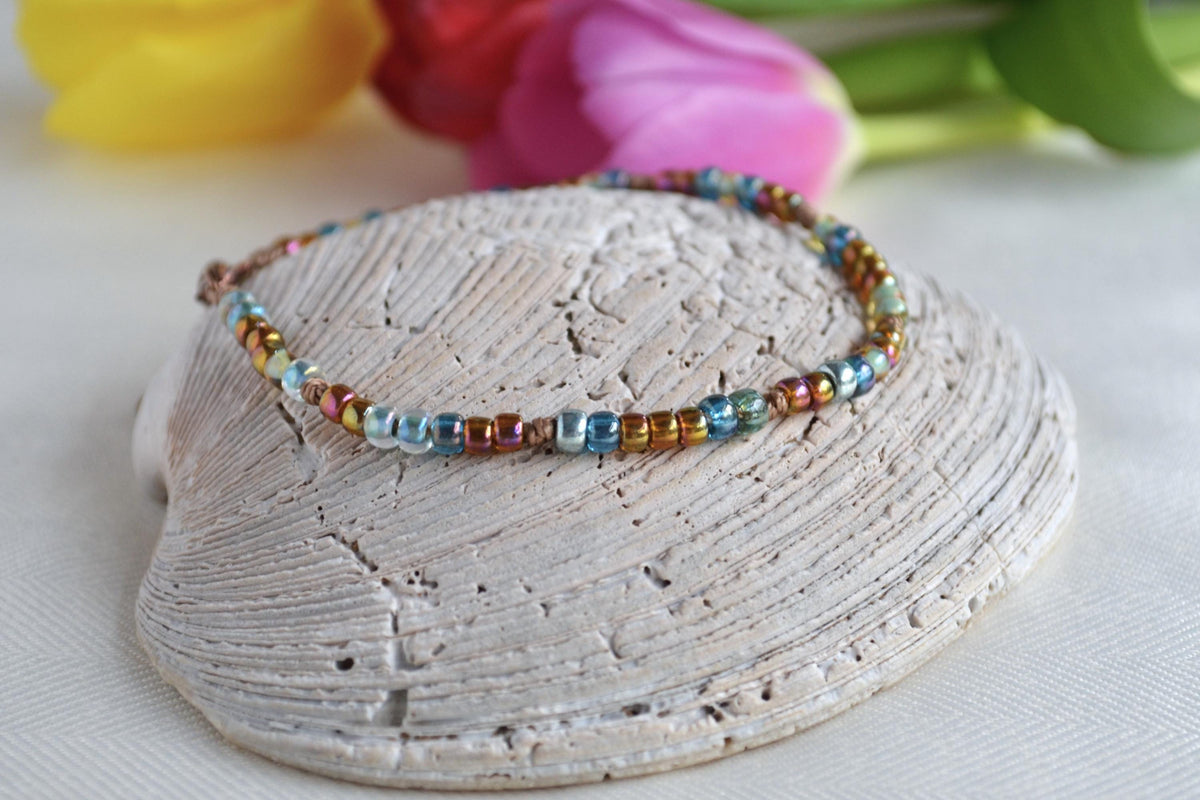 Multicolored beaded ankle bracelet on a shell with flowers in the background