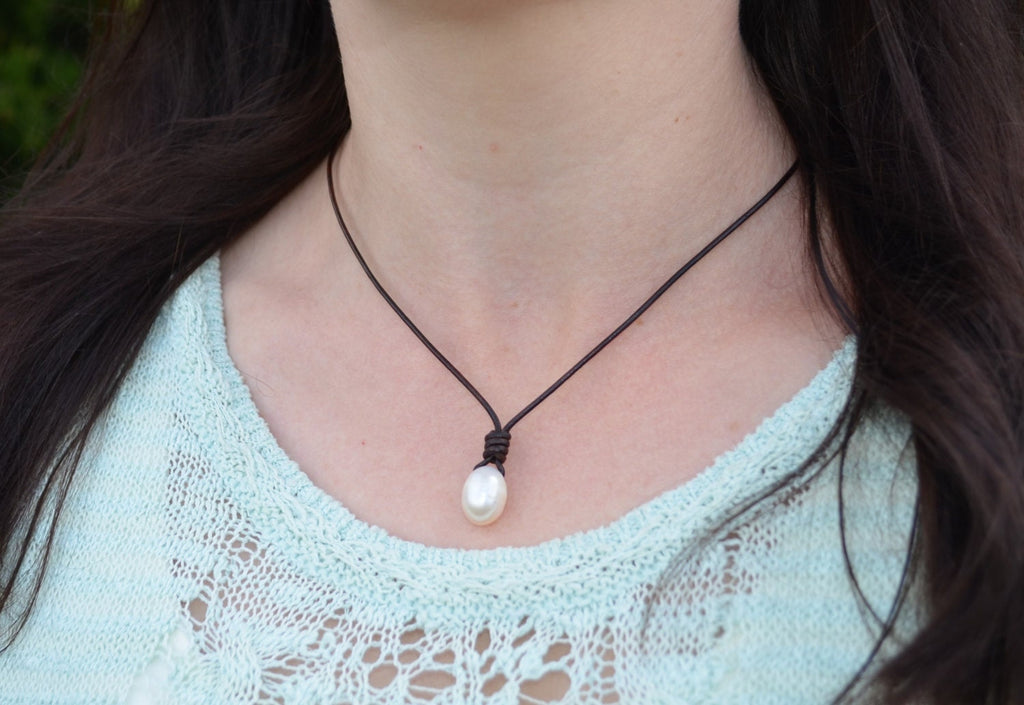 Person wearing a necklace with a pearl pendant, blurred background