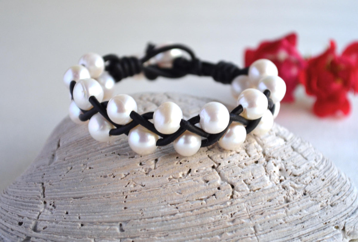 Pearl bracelet with black cord on a textured surface with red flowers in the background