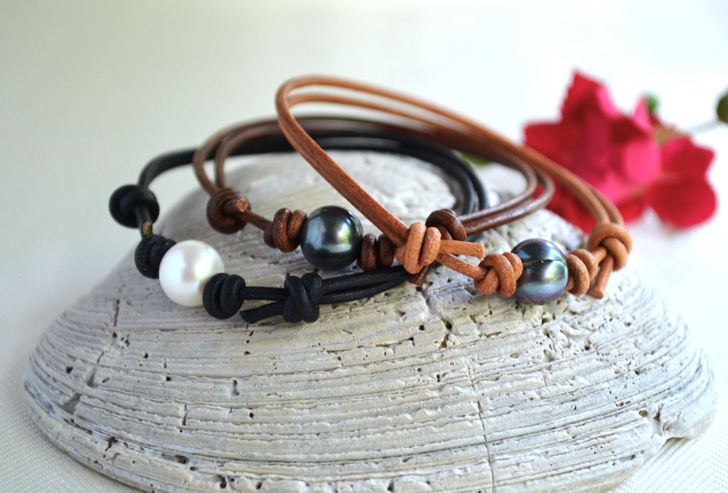 Three leather bracelets with beads on a textured surface with a red flower in the background