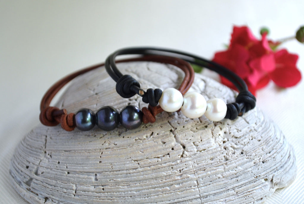Two beaded bracelets on a textured surface with red flowers in the background